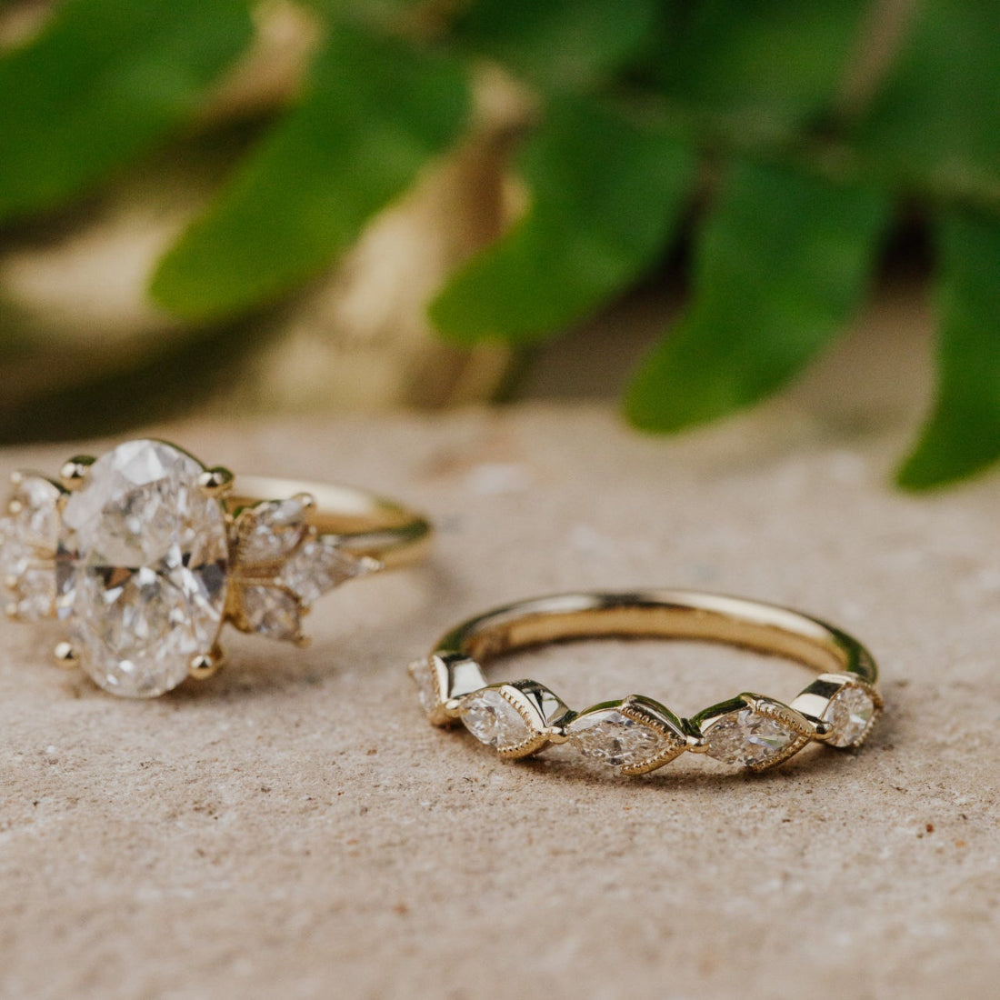 Two gold rings with diamond  on a textured surface with green leaves in the background