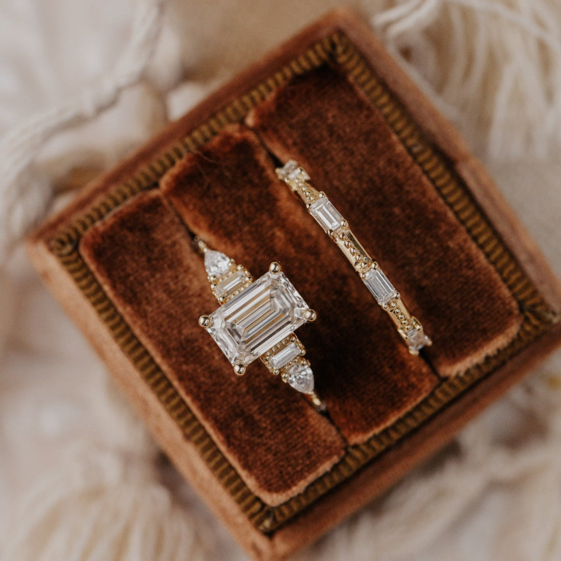 Two diamond rings on a brown velvet cushion with a blurred white background