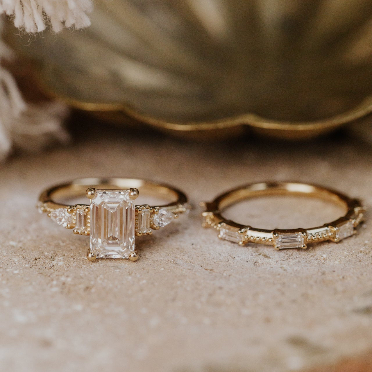 One gold diamond emerald cut ring with a diamond band on a textured surface.