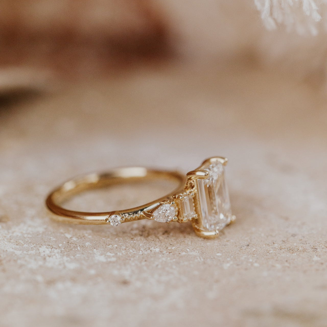 Gold ring with a large emerald cut diamond and smaller diamond side stones on a beige surface