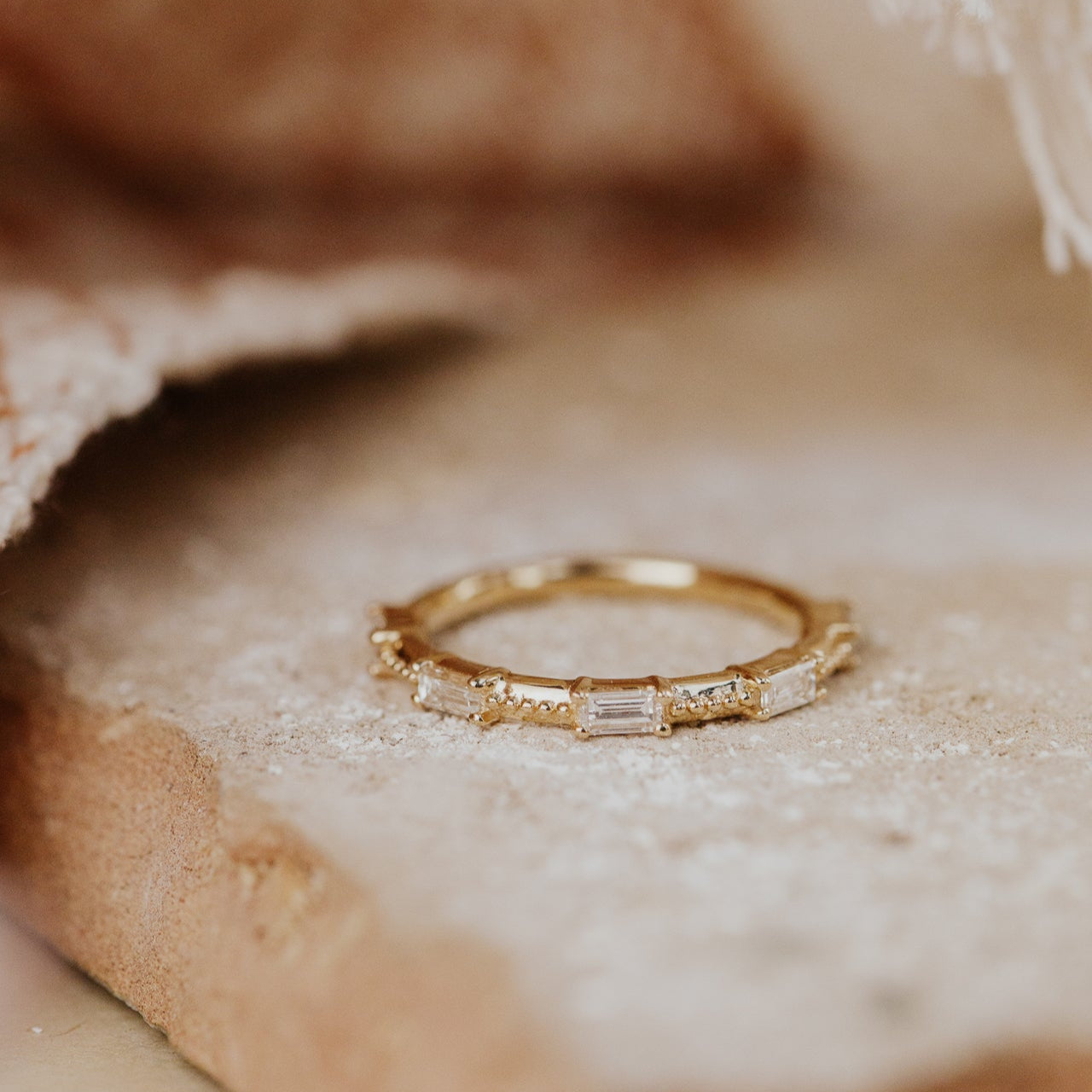 Gold band with diamonds on a textured beige surface