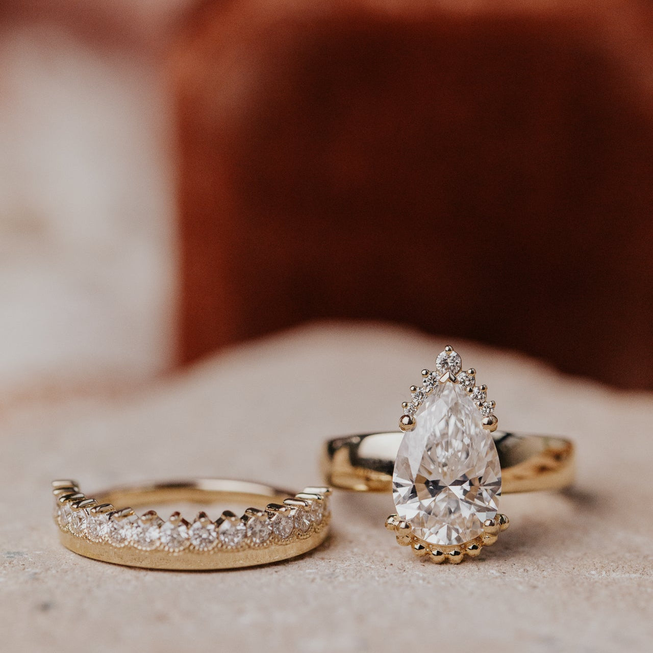 Gold ring with a diamond band and another ring with pear-shaped diamond on a soft surface.