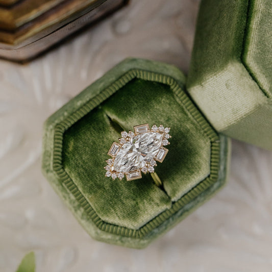 Diamond halo ring in a green velvet box on a textured surface with leaves.