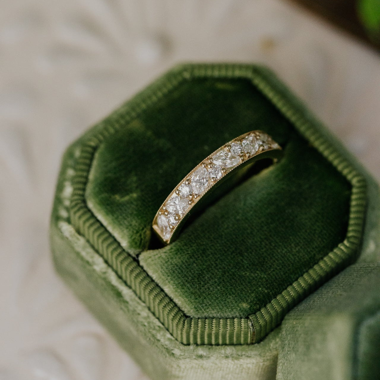 Diamond band in a green velvet box on a textured surface with a plant in the background