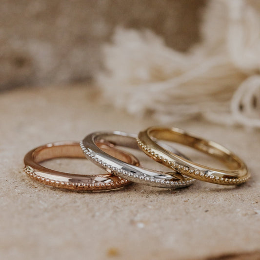 Three gold rings stacked on a textured surface with a blurred natural background