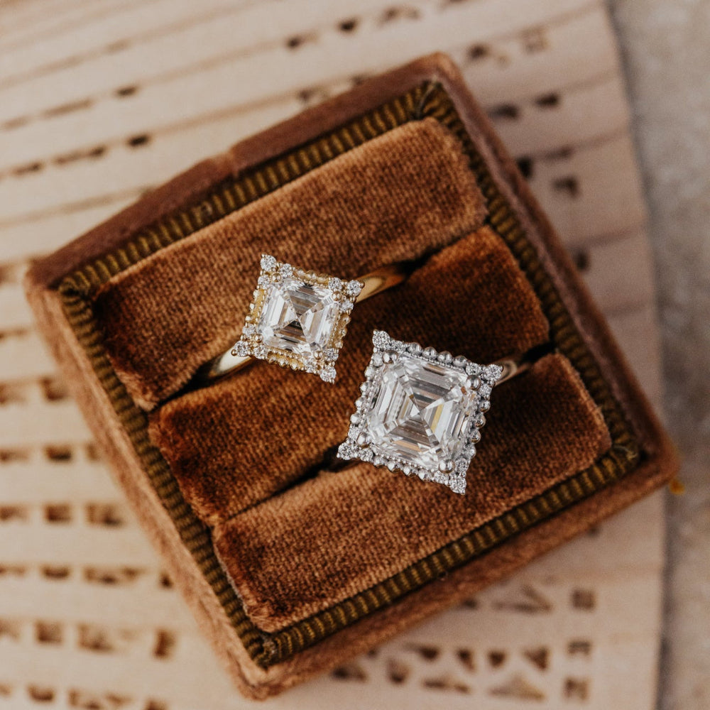 Pair of asscher cut diamond rings s in a brown velvet box on a woven surface