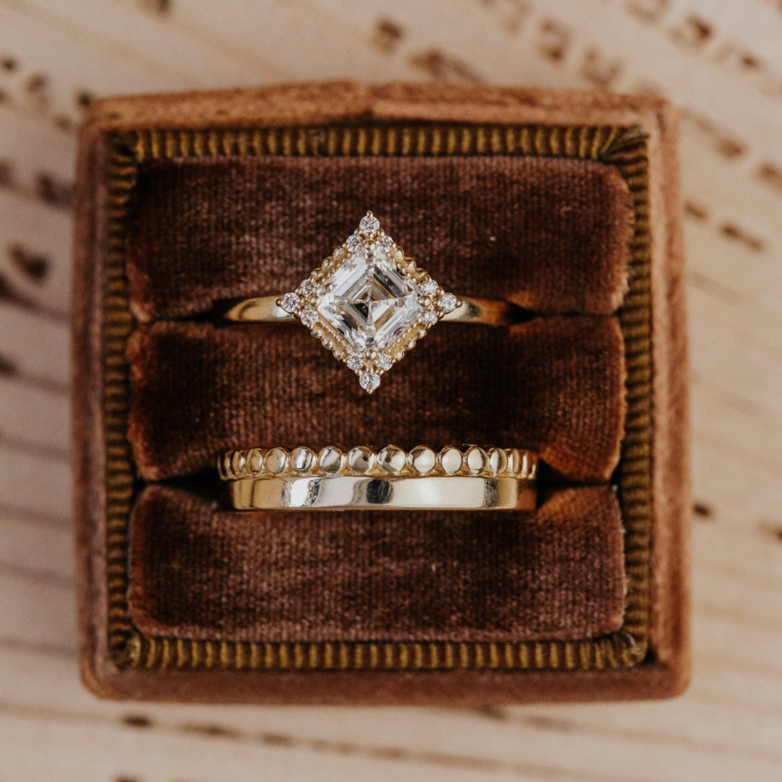 Gold ring with asscher cut diamond in a brown velvet box on a textured surface