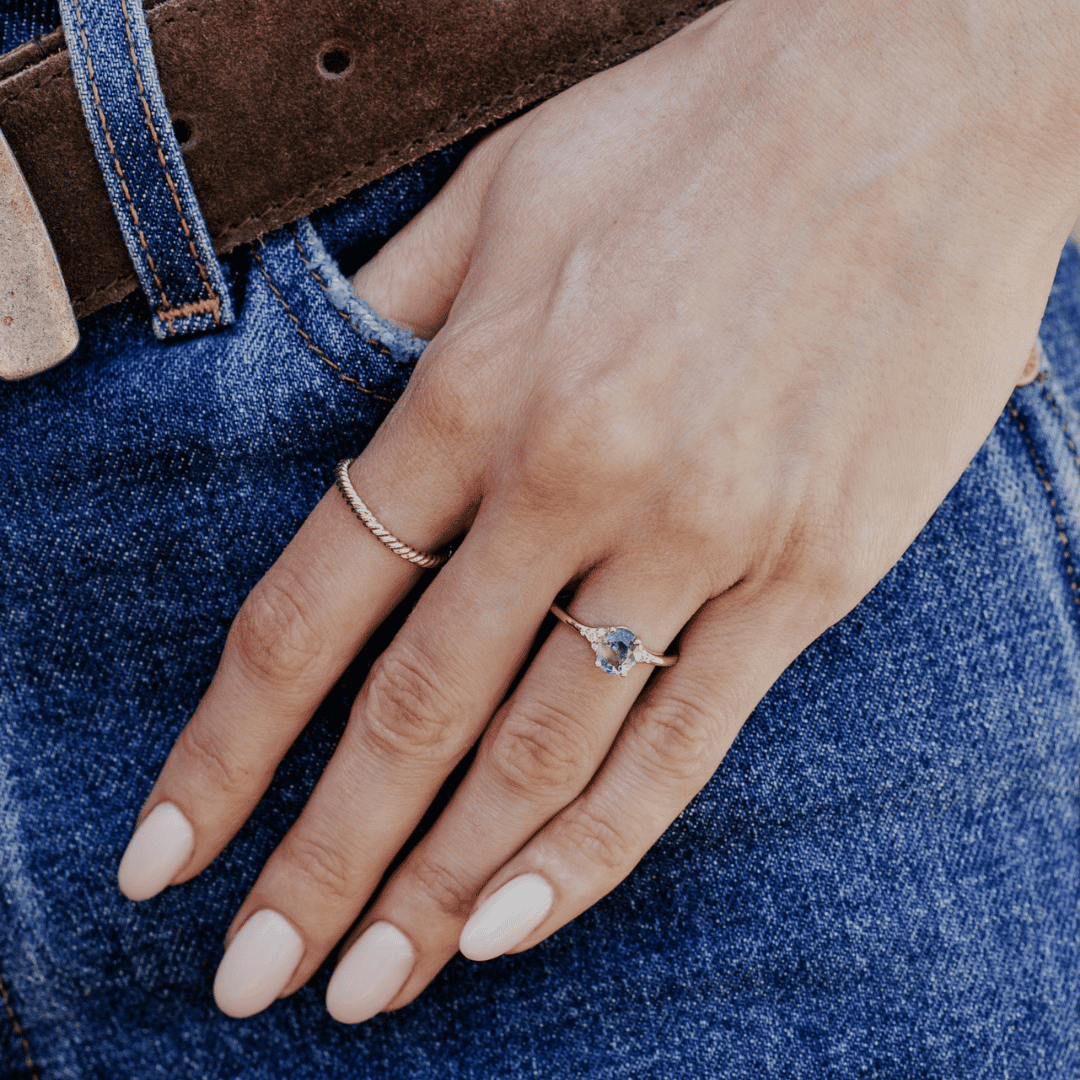 A 14k gold ring featuring a blue sapphire gemstone viewed on the ring finger of a hand model. 