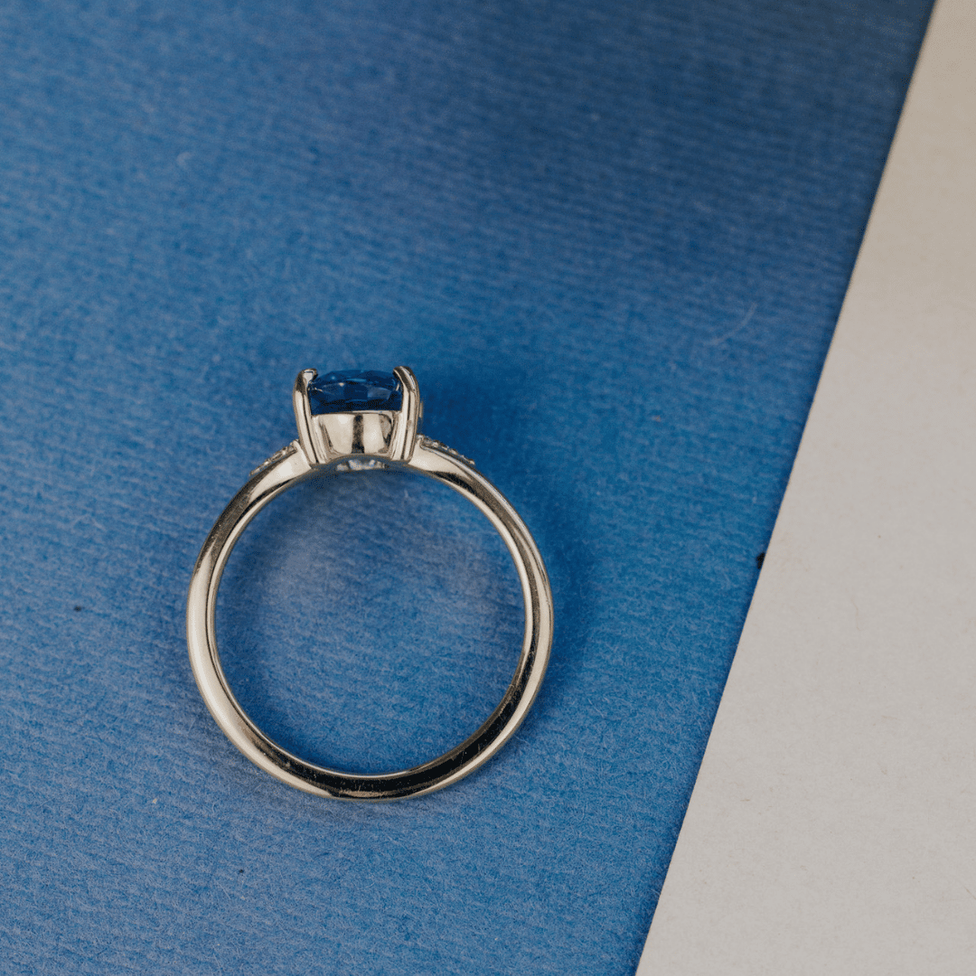 A 14k gold ring featuring a blue sapphire gemstone viewed from the top, displayed on a textured blue surface.