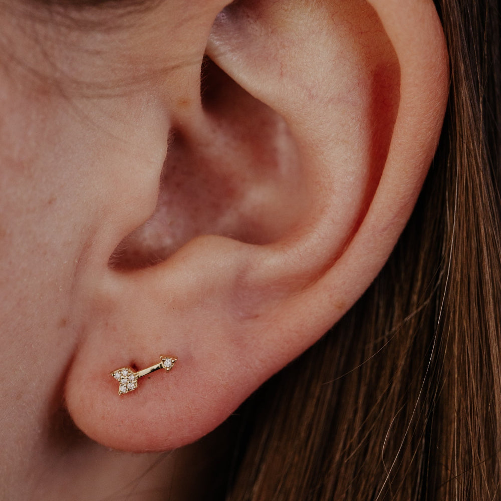 Close-up of an ear with a gold arrow-shaped diamond stud earring.