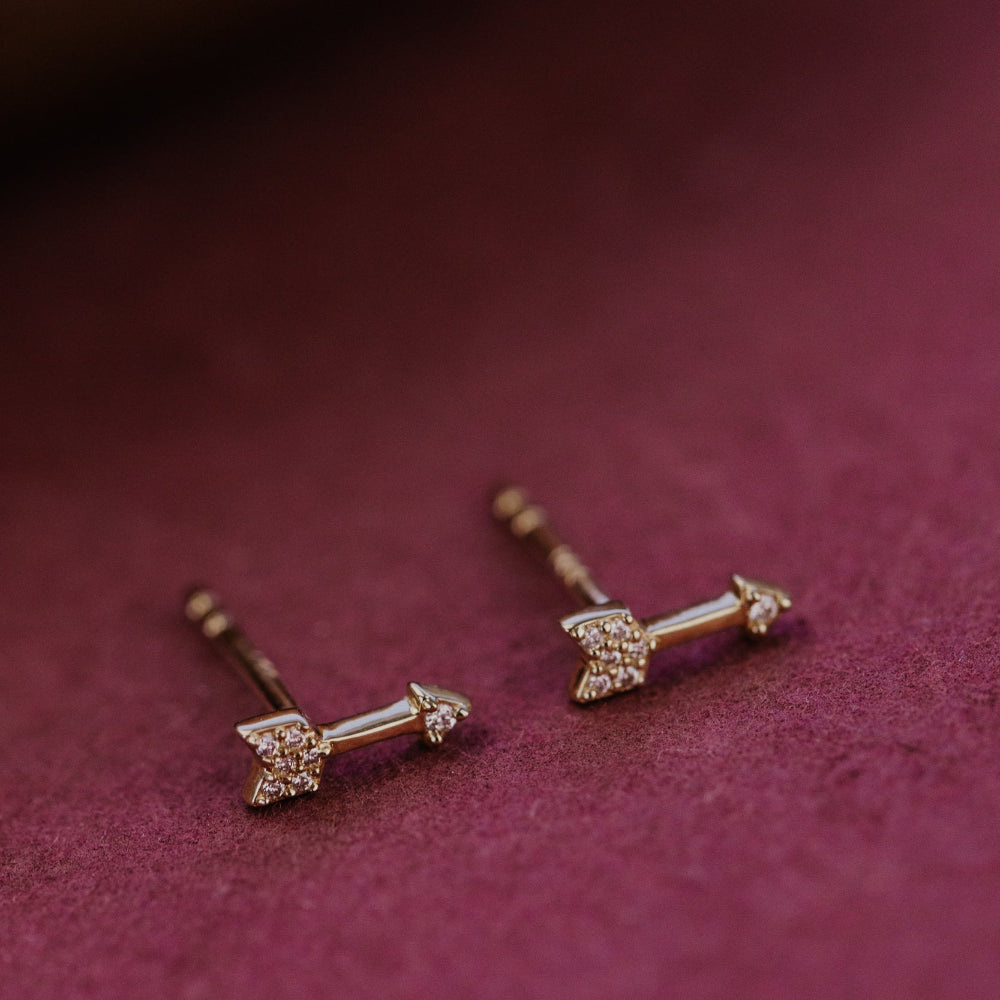 Gold earrings with a diamond on a maroon background.