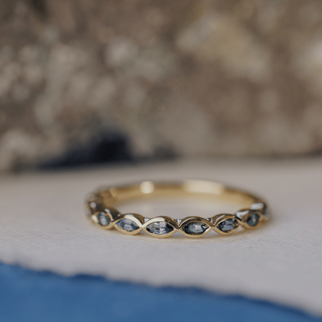 A 14k gold ring featuring blue marquise sapphire gemstones displayed on a white surface with a soft-focus background.