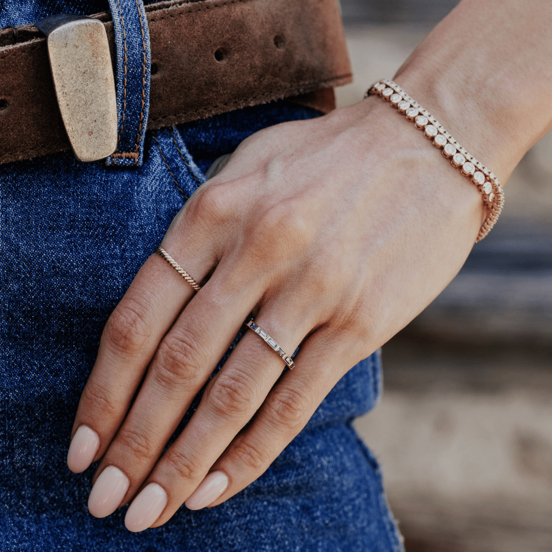 A 14k gold ring featuring blue oval sapphire gemstones displayed on the ring finger of a hand model. 