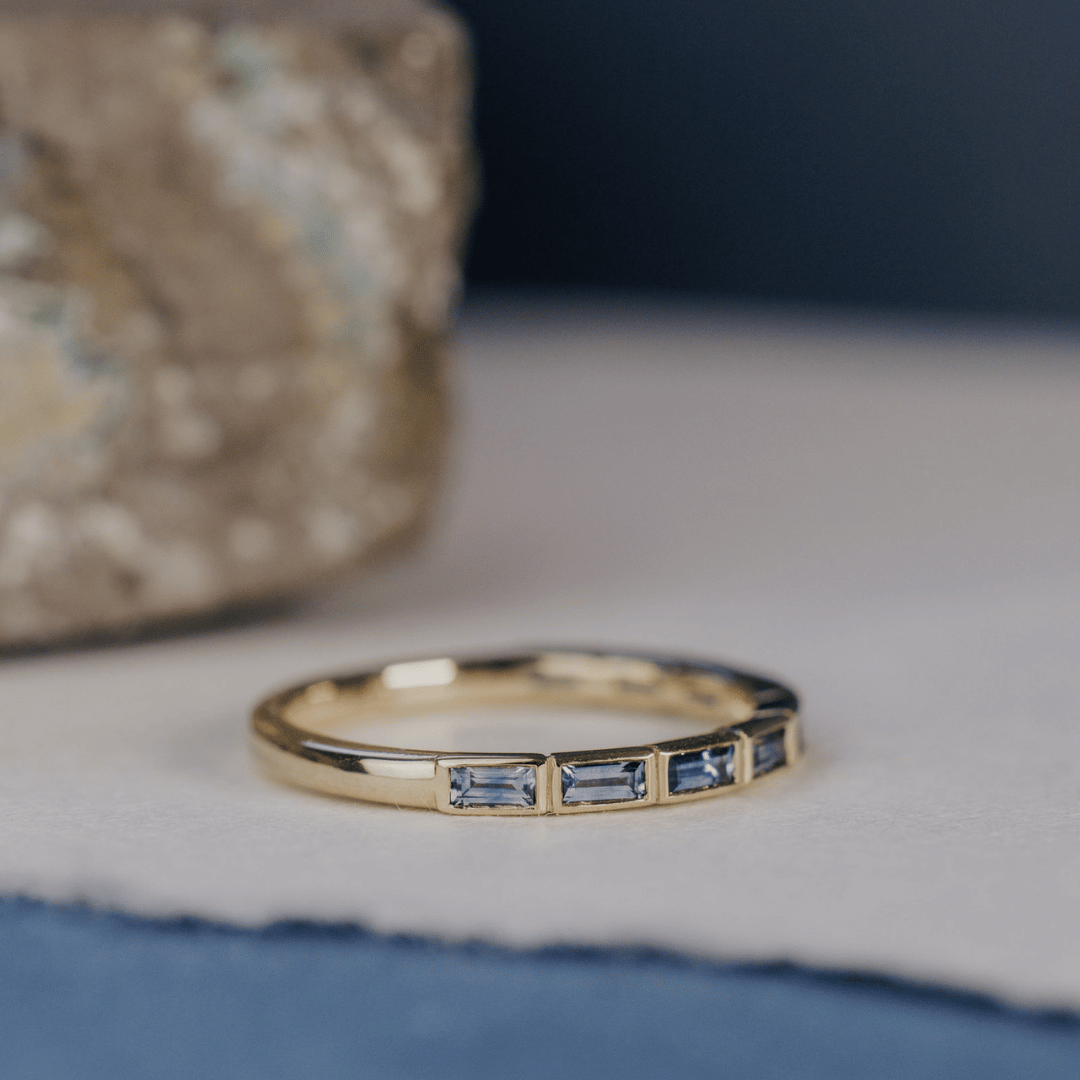 A 14k gold ring featuring blue oval sapphire gemstones displayed on a white surface with a soft-focus background.