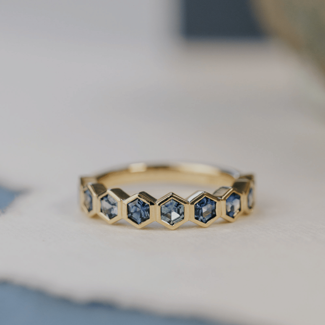 A 14k gold ring featuring blue hexagonal cut sapphire gemstones displayed on a white surface with a soft-focus background.
