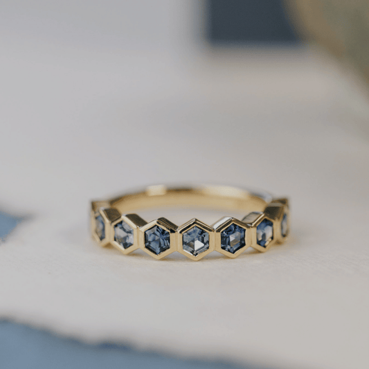 A 14k gold ring featuring blue hexagonal cut sapphire gemstones displayed on a white surface with a soft-focus background.