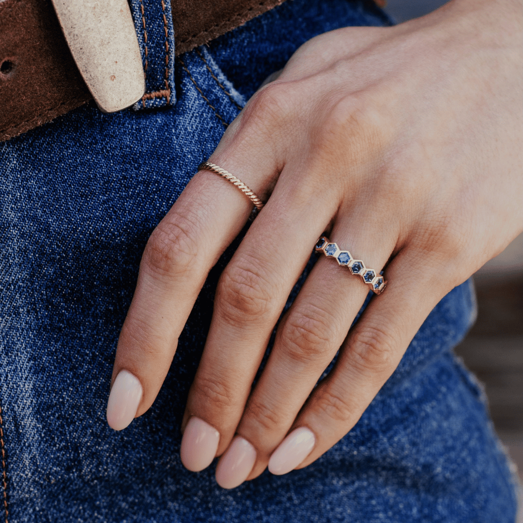 A 14k gold ring featuring blue hexagonal cut sapphire gemstones from an angled view, displayed on the ring finger of a hand model.