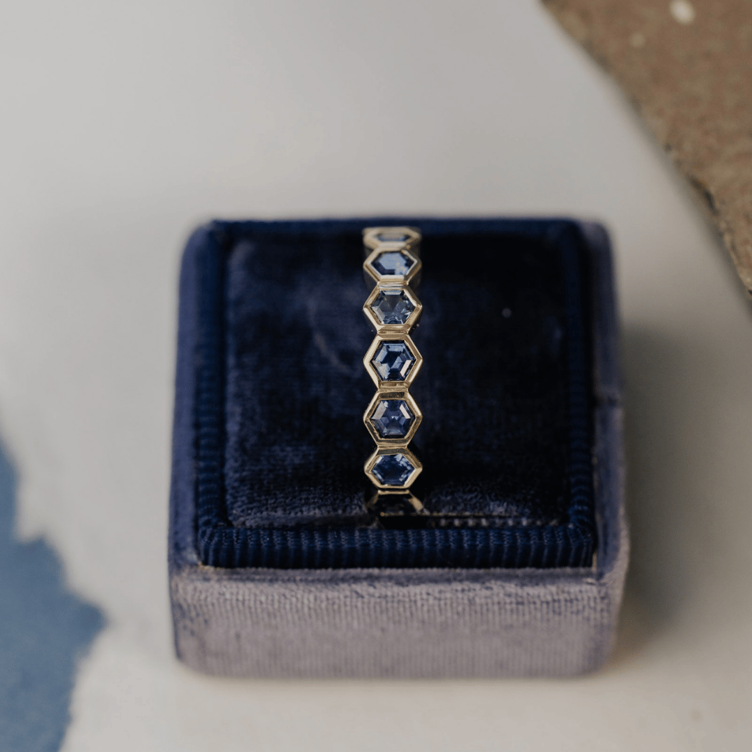 A 14k gold ring featuring blue hexagonal cut sapphire gemstones from a top view, displayed in a ring box with a soft-focus background.