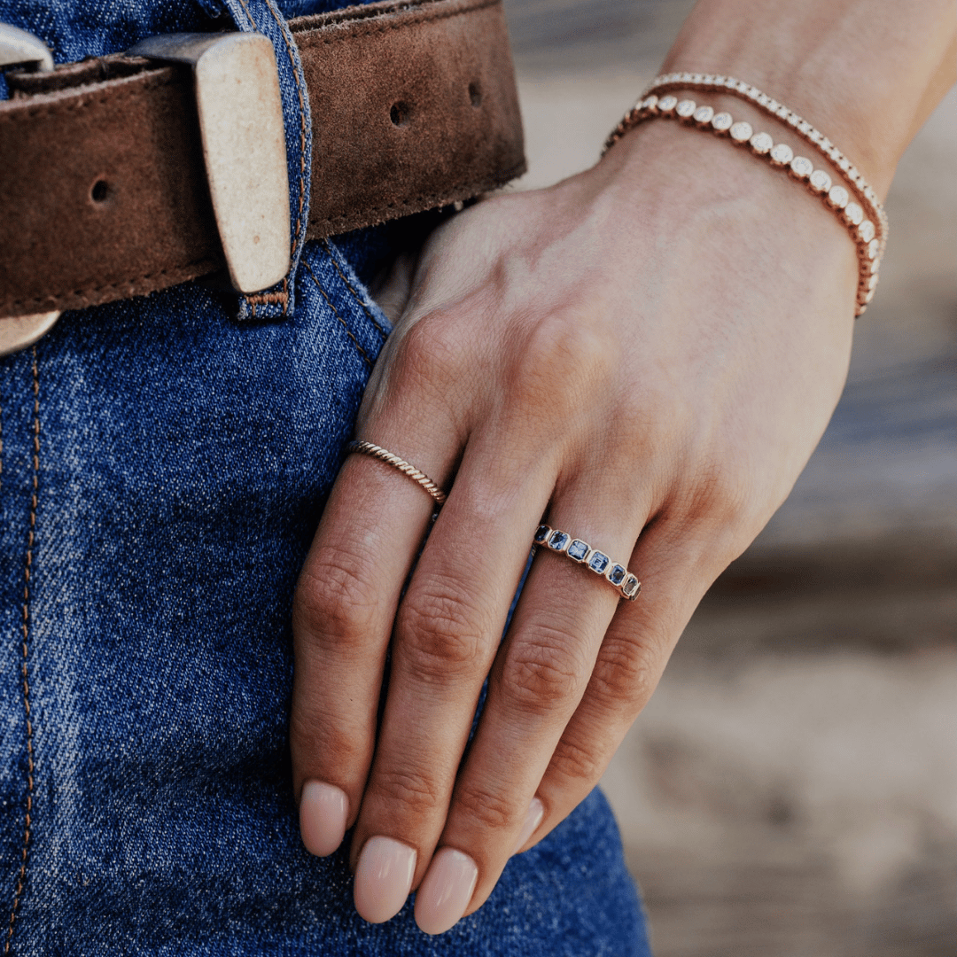 A 14k gold ring featuring asscher cut, blue sapphire gemstones, displayed on the ring finger of a hand model. 
