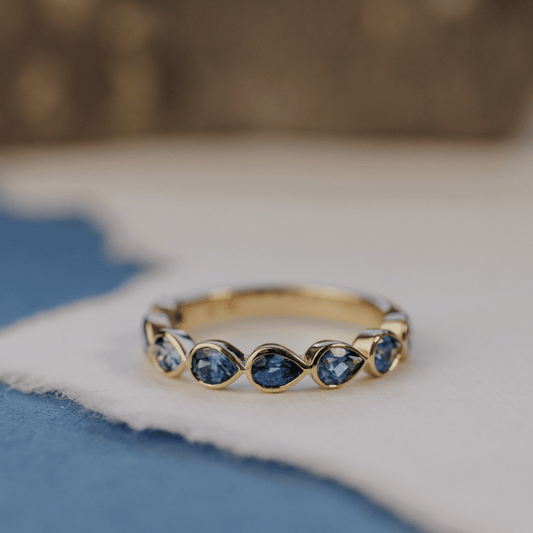 A 14k gold ring featuring blue pear sapphire gemstones displayed on a white surface with a soft-focus background.