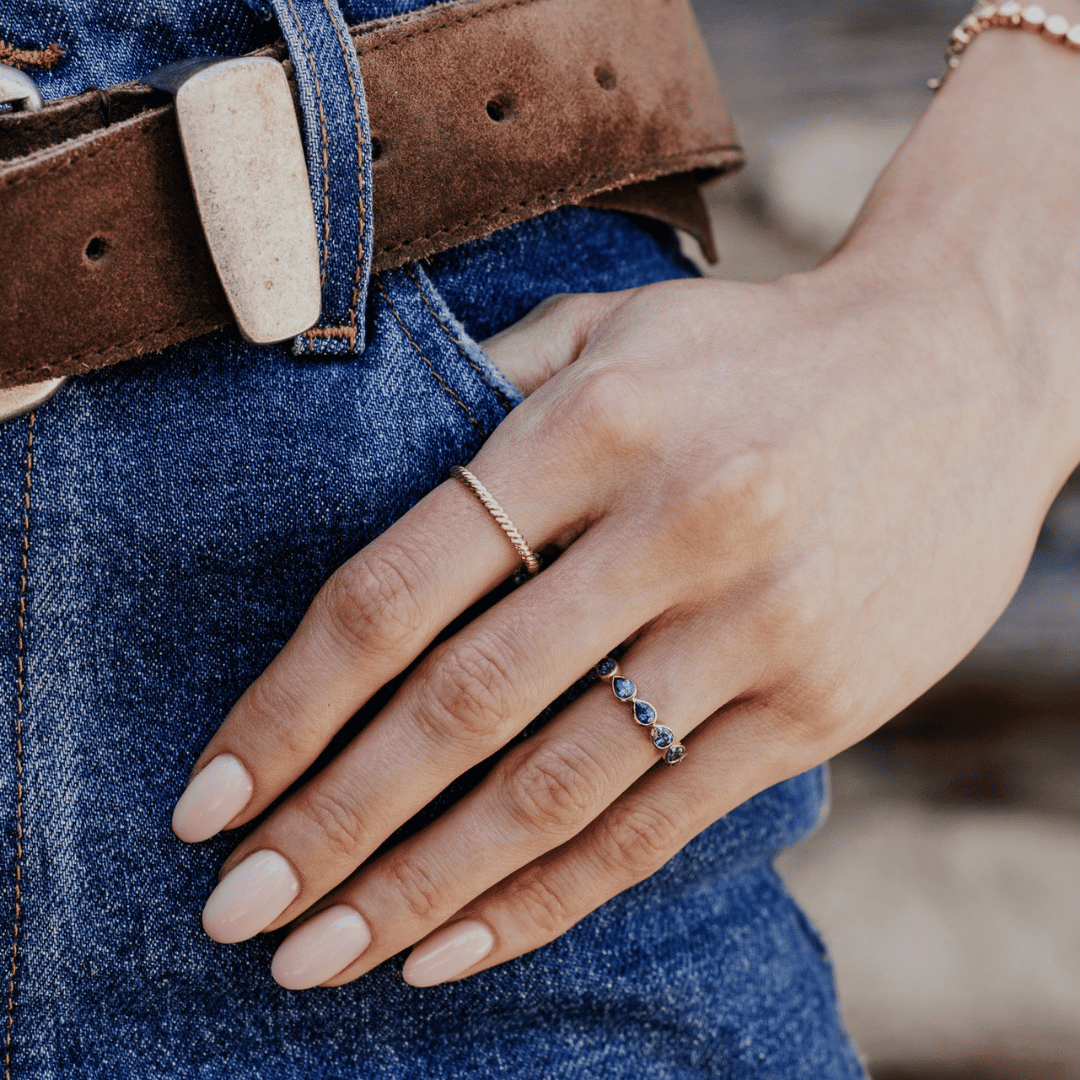 A 14k gold ring featuring blue pear sapphire gemstones displayed on the3 ring finger of a hand model. 