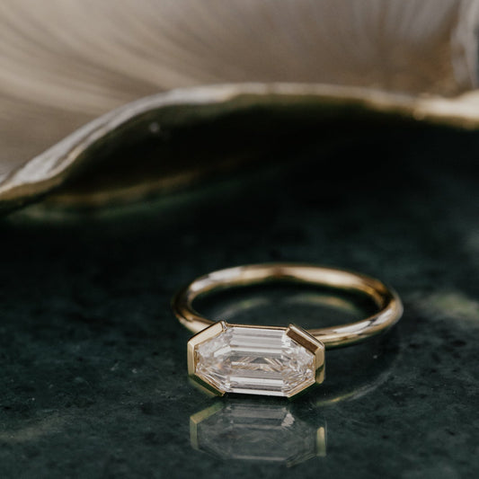 Gold ring with a lab grown diamond on a dark surface.