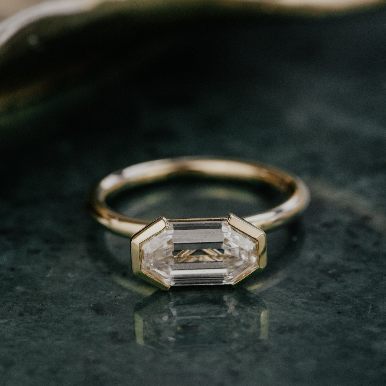Gold ring with a lab grown diamond on a dark surface.