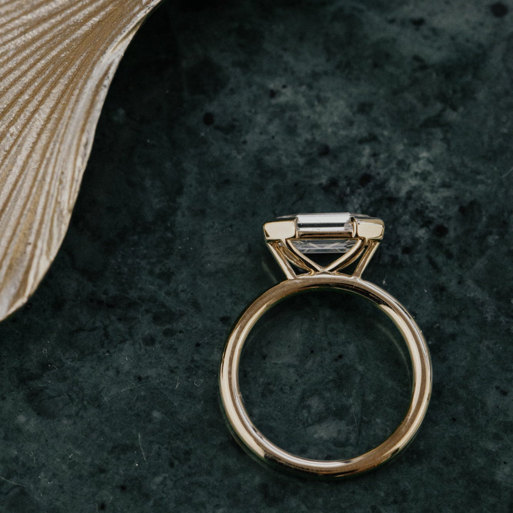 Gold ring with a diamond on a textured dark surface.