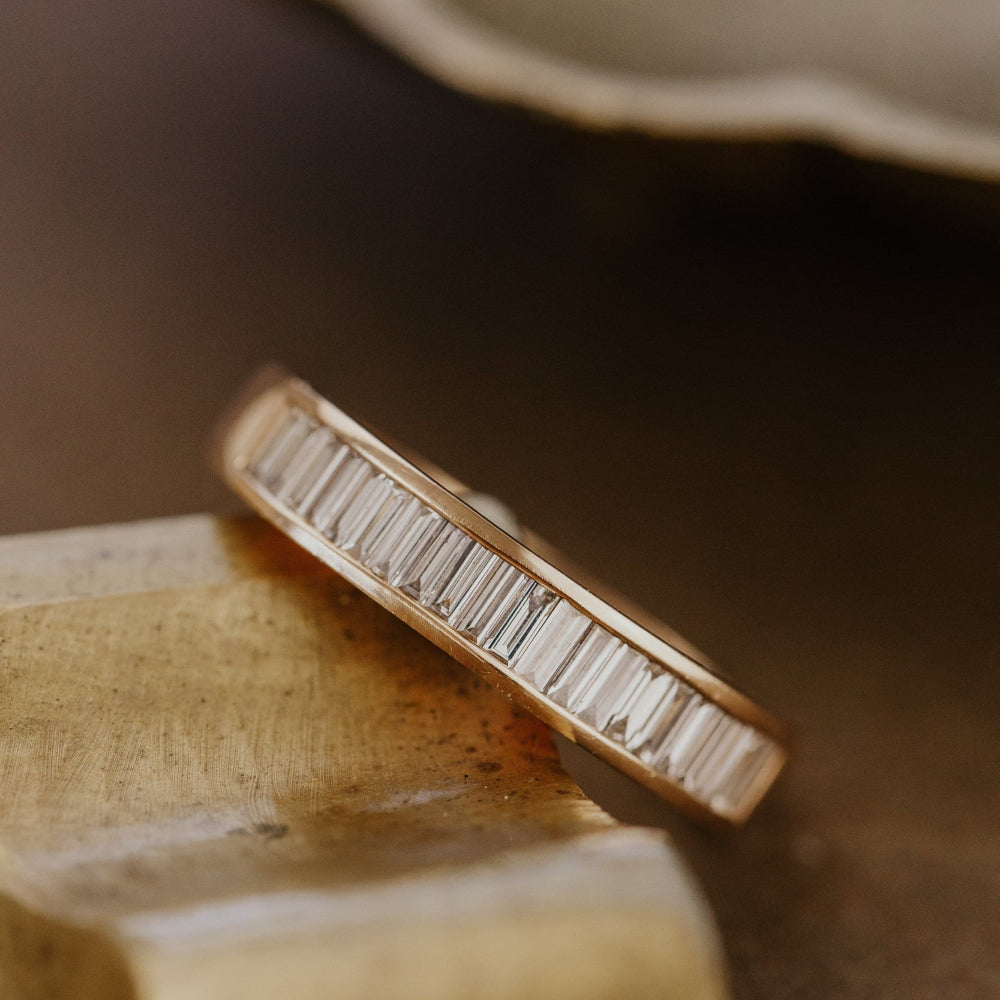 Rose gold wedding band with baguette diamonds on a wooden surface.