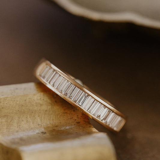 Rose gold wedding band with baguette diamonds on a wooden surface.