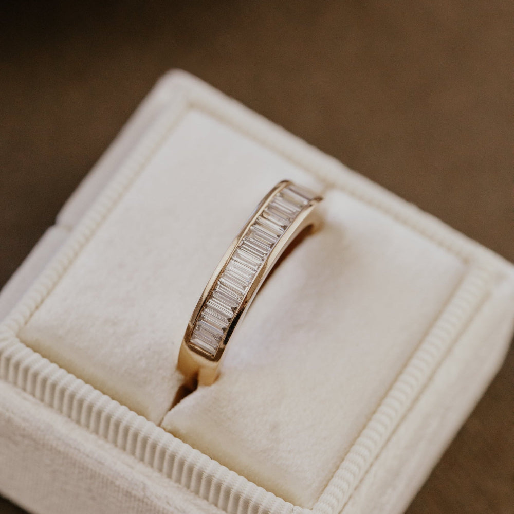 Rose gold wedding band with diamond accents in a jewelry box on a brown background.