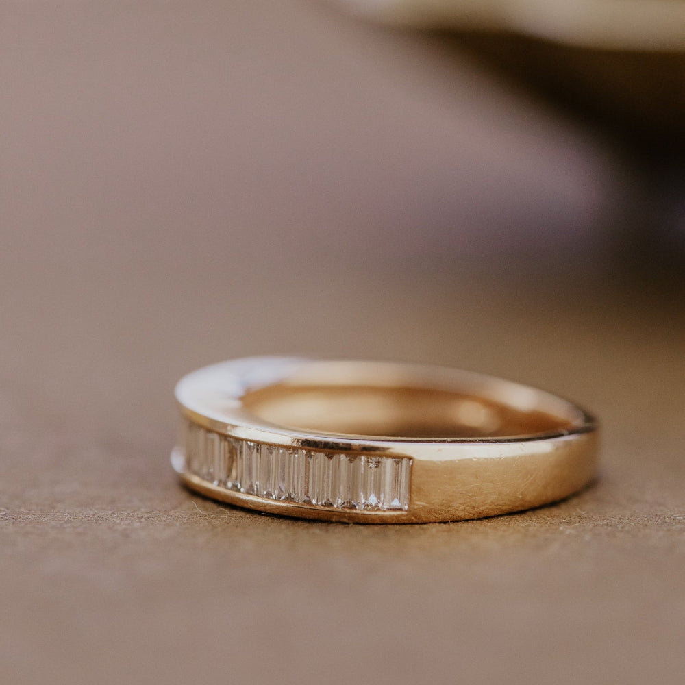 Rose Gold wedding band with diamond accents on a beige surface.