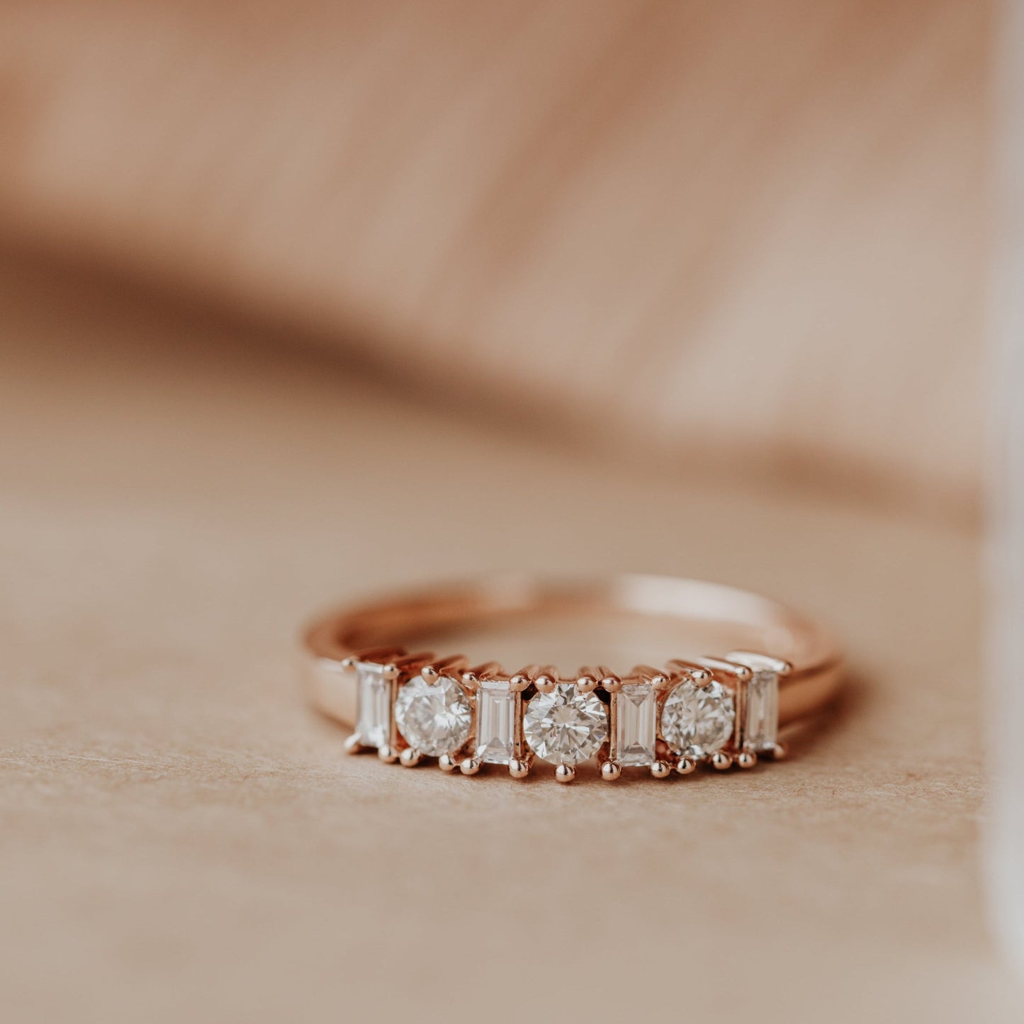 14k Rose gold wedding band with diamonds on a beige background.