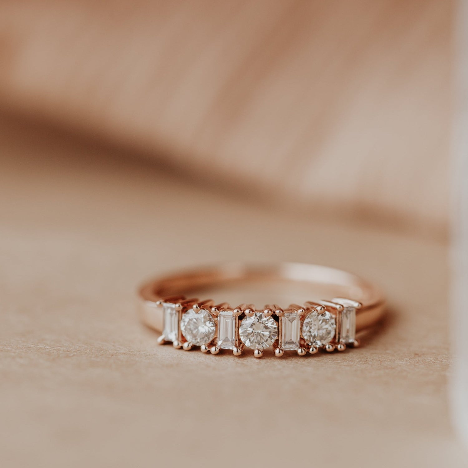 14k Rose gold wedding band with diamonds on a beige background.