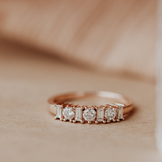14k Rose gold wedding band with diamonds on a beige background.
