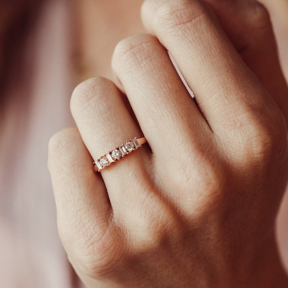 Close-up of a hand wearing a rose gold wedding band with natural diamonds.