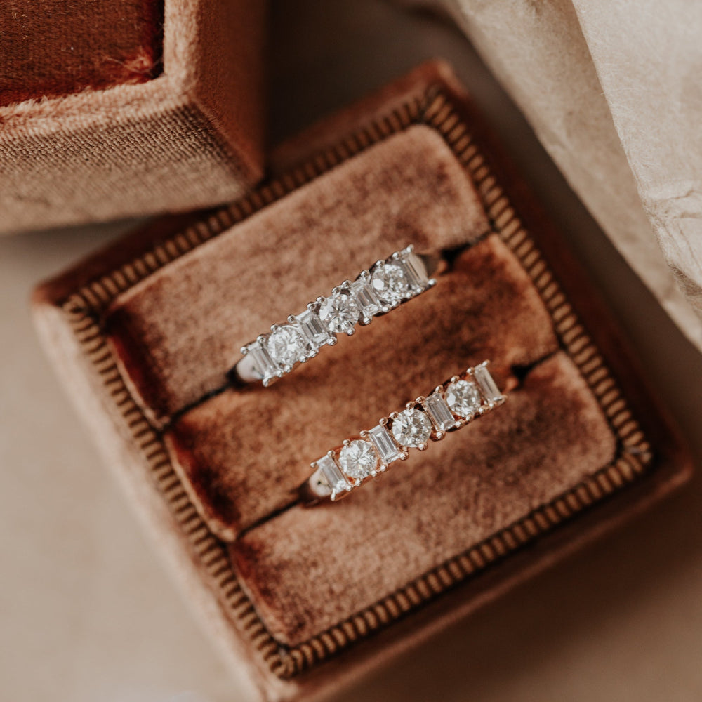 Two diamond wedding bands in a brown velvet box on a soft beige background.