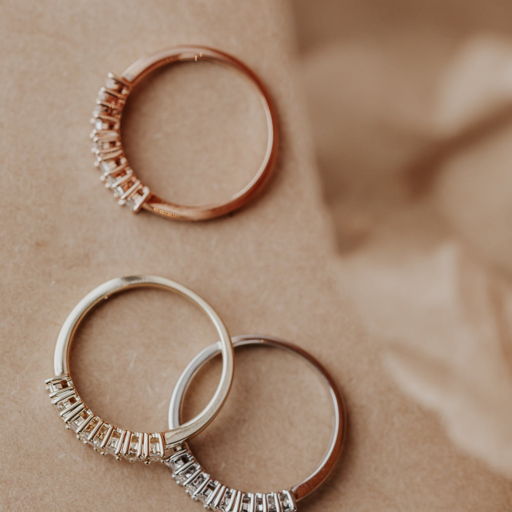 Three diamond wedding bands in 14k yellow, white, and rose gold on a beige fabric background.