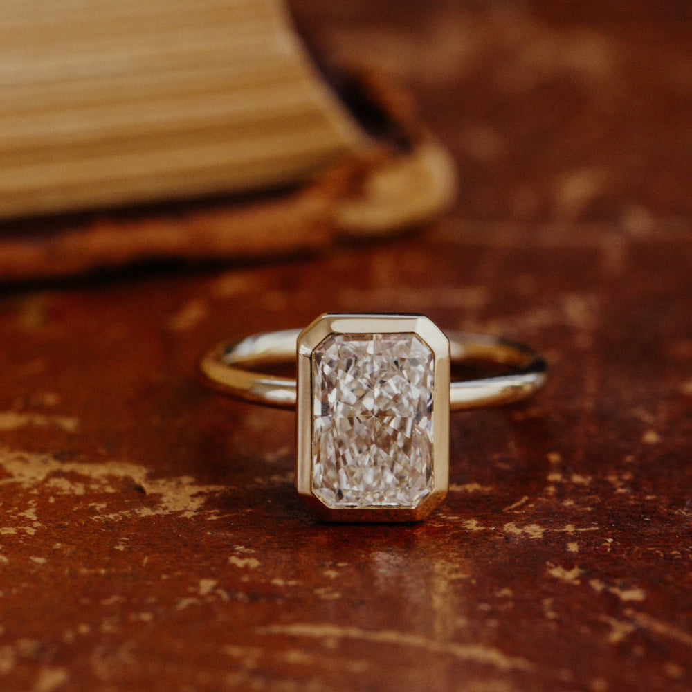 The Bailey radiant cut ring with a lab grown diamond on a wooden surface.