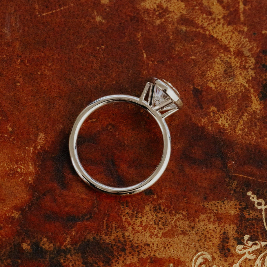 The Bailey white gold bezel set ring with a oval lab grown diamond on an old, textured brown book.