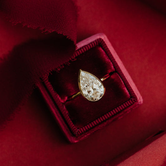The Bailey pear-shaped diamond ring in a red velvet box on a red fabric background.
