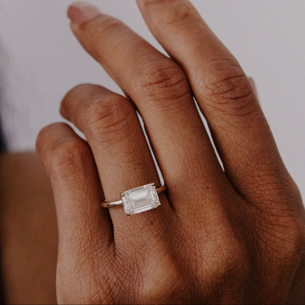 Close-up of a hand wearing the Bennett 2.52 ct emerald cut lab grown diamond ring with a blurred background.