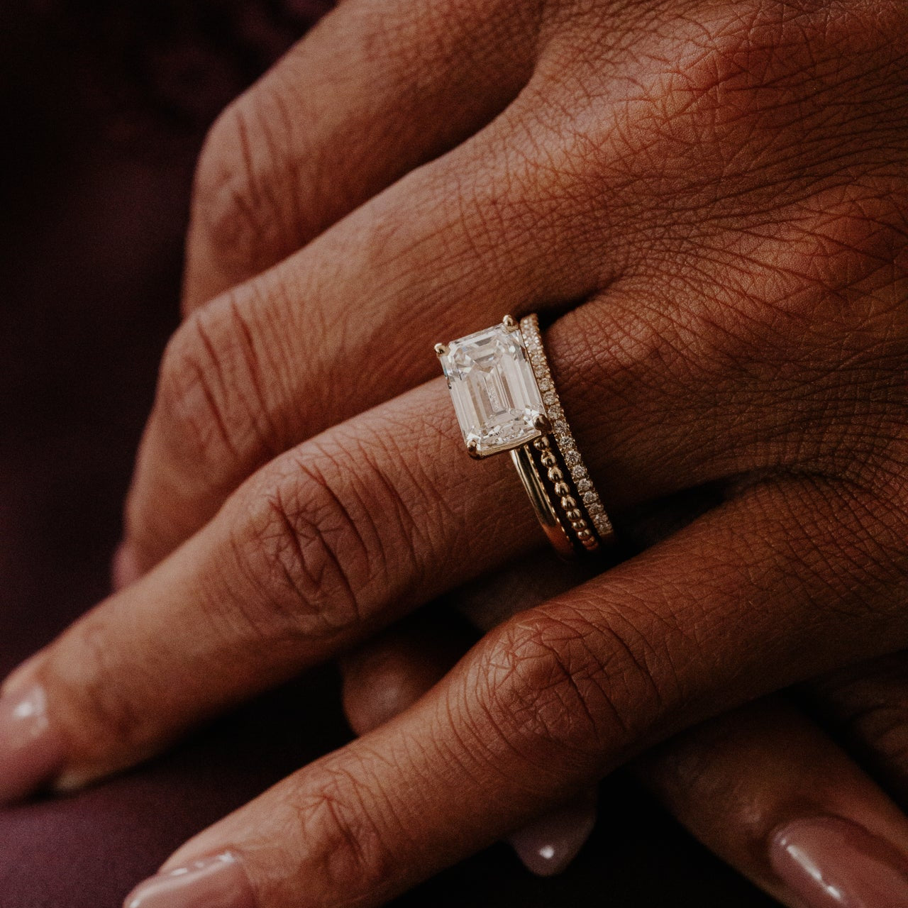 Close-up of a hand wearing the Bennett emerald cut solitaire diamond ring on a dark background.
