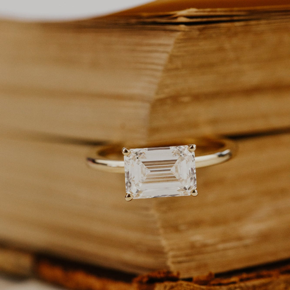  The Bennett emerald cut solitaire diamond ring on a wooden surface.