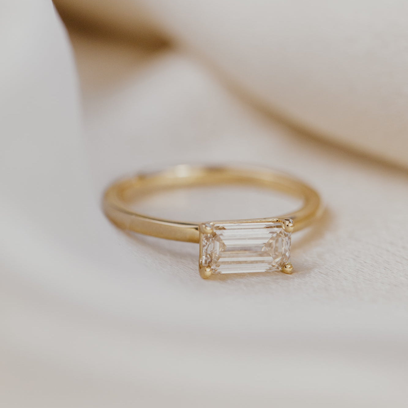Gold engagement ring with a emerald cut champagne diamond on a soft beige background.