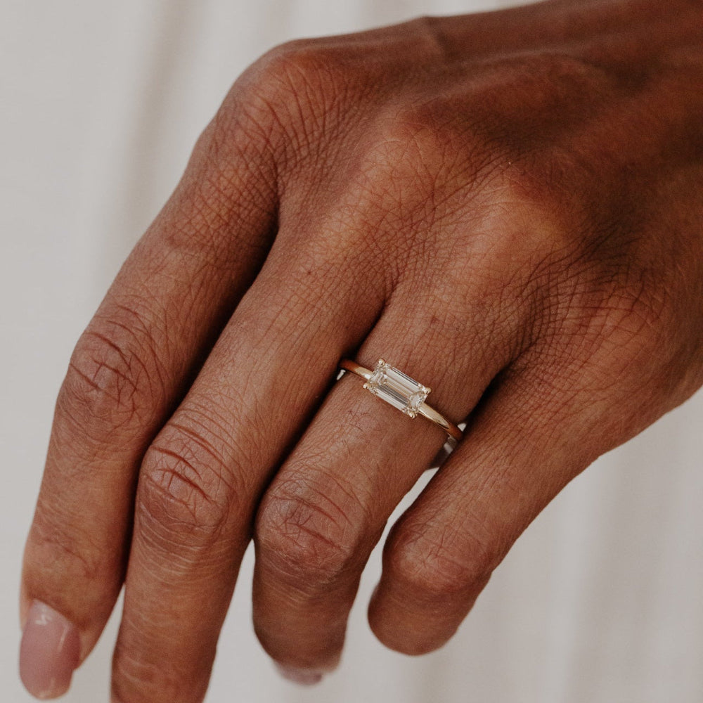Hand wearing a gold engagement ring with a champagne diamond stone on a neutral background.