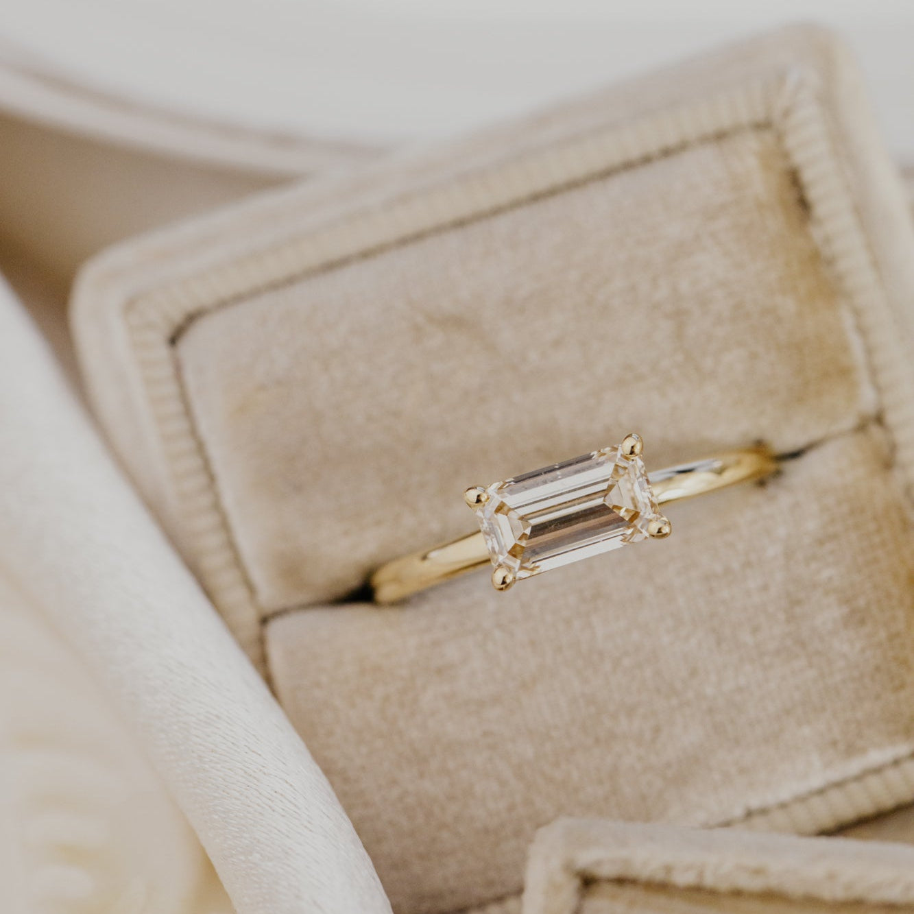 Gold engagement ring with a champagne diamond in a beige jewelry box.