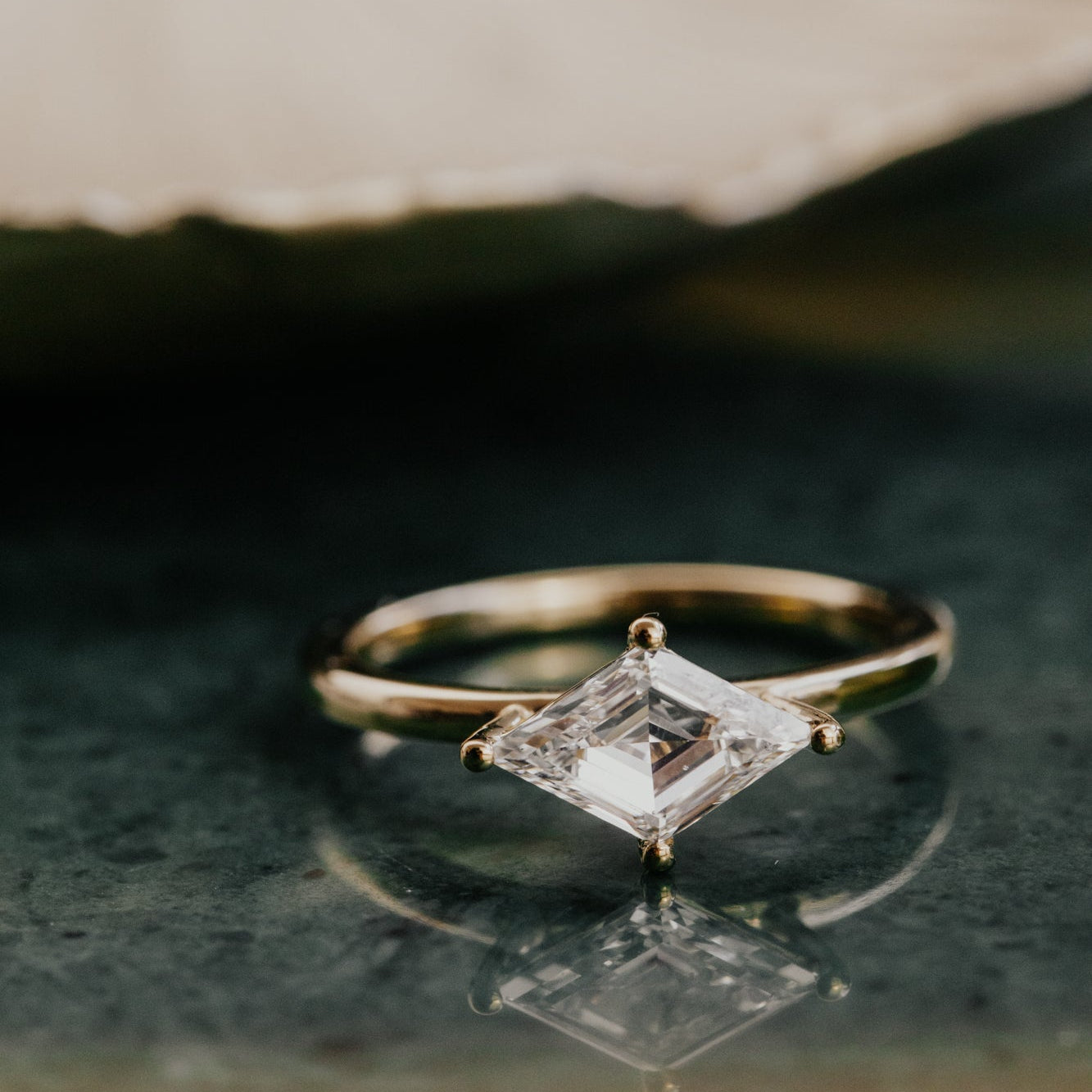 Gold ring with a lozenge diamond on a dark surface.
