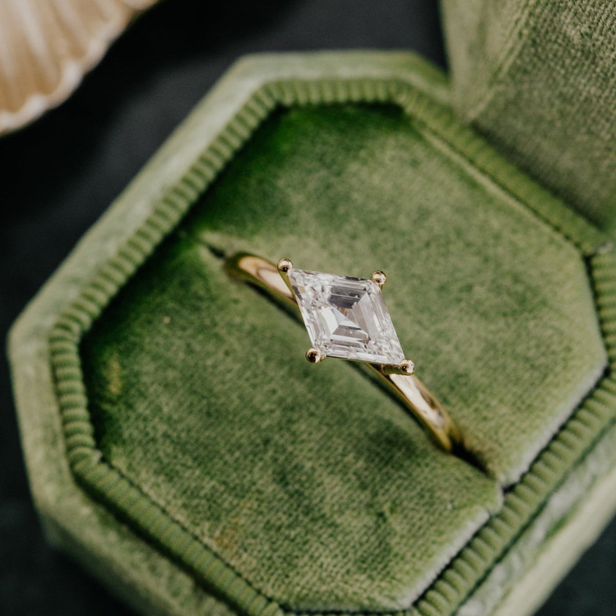 Diamond ring in a green velvet box with a shell in the background.