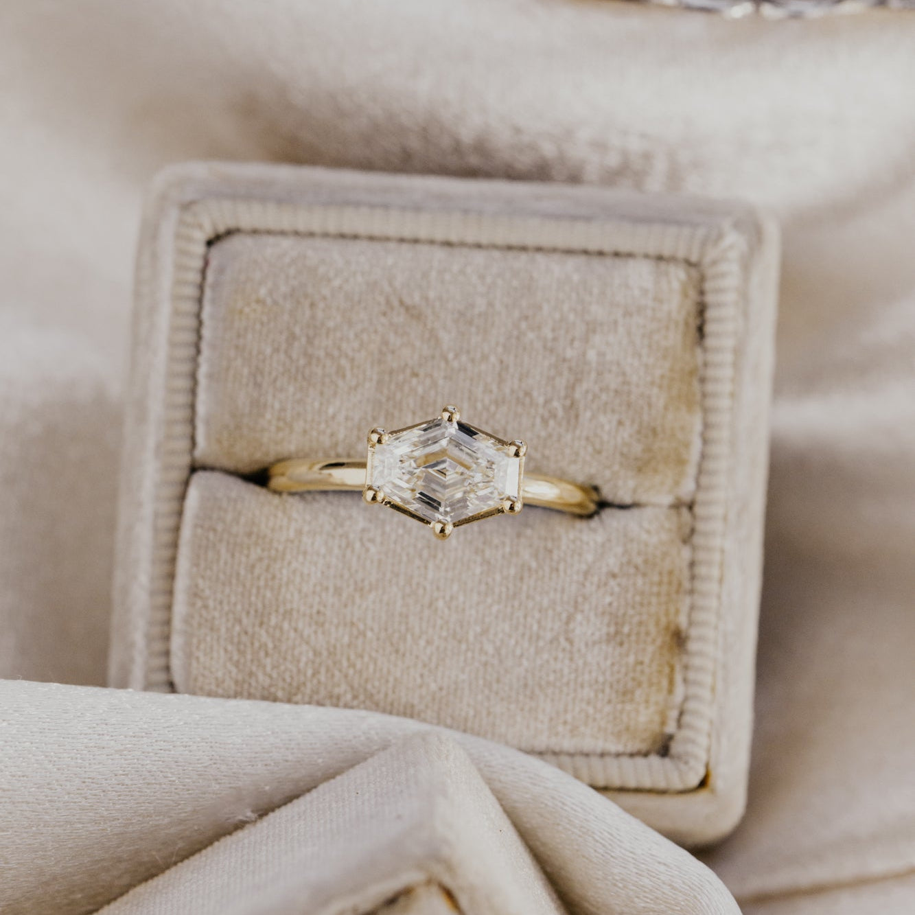 Gold ring with a champagne diamond in a beige jewelry box on a soft beige fabric background.